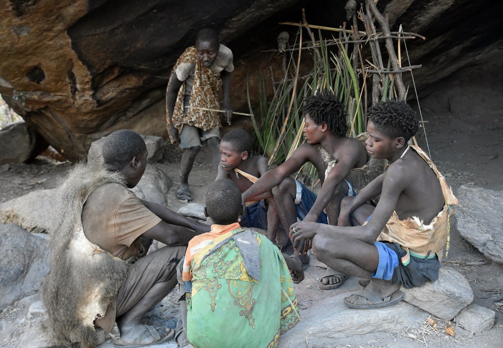 Photograph of a group of Hadzabe men resting under a rock formation.